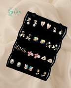 Black earring holder with various earrings on a beige fabric background, featuring the DIVA brand.
